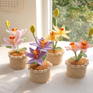 May include: A collection of handmade crochet flowers in small pots. The flowers are in various colors, including pink, yellow, and purple, with green stems and leaves. The pots are a light beige color.