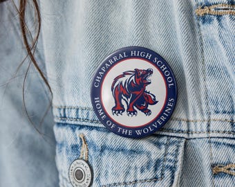 May include: A circular pinback button featuring a white center with a red and blue wolverine graphic. The dark blue border contains the white text "CHAPARRAL HIGH SCHOOL" at the top and "HOME OF THE WOLVERINES" at the bottom, pinned to denim.