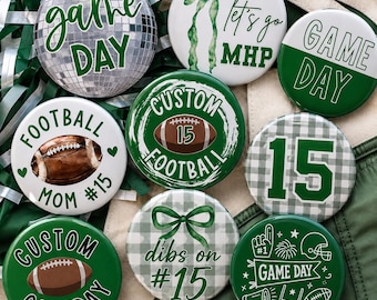 May include: A collection of nine round pinback buttons featuring green and white designs with football themes. Text includes game day, let's go MHP, football mom #15, custom football 15, 15, custom gameday, and dibs on #15, alongside football and cheer graphics.