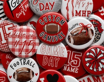 May include: A collection of round pin-back buttons featuring various football-themed designs in red, white, and brown. Graphics include a football, a disco ball, a red gingham pattern, a pom-pom, and text such as Game Day, Football Mom #15, and Phantoms.