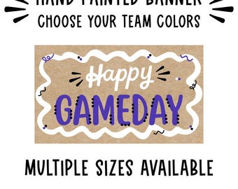 May include: A rectangular brown paper banner featuring the white text Happy and the purple text GAMEDAY. The banner is framed by a white wavy border with small purple and black decorative accents. Text above reads HAND PAINTED BANNER CHOOSE YOUR TEAM COLORS and text below reads MULTIPLE SIZES AVAILABLE.