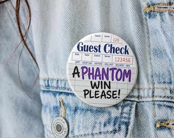 May include: A round pinback button featuring a white guest check design with blue lines and headers. The text reads Guest Check, 126, 123456, APPT, SOUP/SAL, ENTREE, VEG/POT, DESSERT, BEV, and the purple and black text A PHANTOM WIN PLEASE!