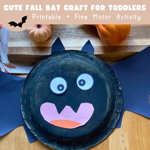 May include: A black paper plate bat craft with white eyes, a pink mouth, and an orange tongue. The bat has dark blue paper wings and ears. The text "CUTE FALL BAT CRAFT FOR TODDLERS" is at the top.