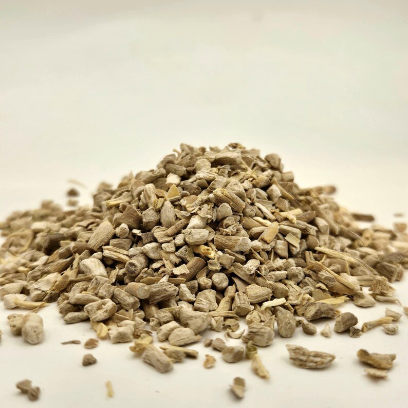 May include: A pile of chopped, light brown, dried plant material. The pieces vary in size and shape, with a mix of textures. The background is a plain, off-white color, providing a neutral backdrop for the product.