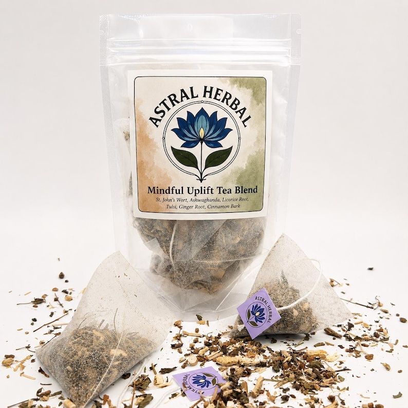 May include: A clear plastic bag of Astral Herbal Mindful Uplift Tea Blend with a white label featuring a blue lotus flower design. Two tea bags and loose tea leaves are scattered around the bag. The label lists ingredients like St. John's Wort and Ginger Root.