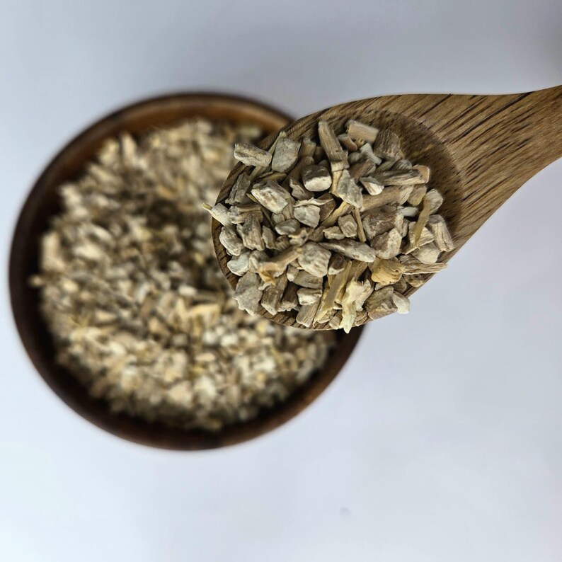 May include: A wooden spoon holds a portion of light brown, chopped herbs or spices, with a wooden bowl filled with similar pieces in the background. The items are set against a white background.