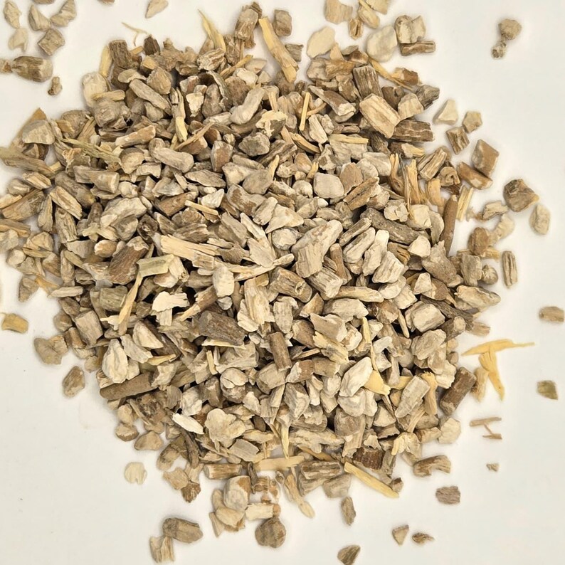 May include: A pile of chopped, dried, light brown and beige herbal pieces. The pieces vary in size and shape, with some appearing like small sticks and others more like irregular chunks. The background is a plain white surface.