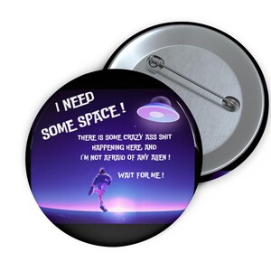 Peut inclure: Un bouton rond avec un design humoristique. Le bouton présente une scène spatiale violette et bleue avec une personne courant vers un OVNI. Le texte sur le bouton se lit "I NEED SOME SPACE!" et "WAIT FOR ME!"