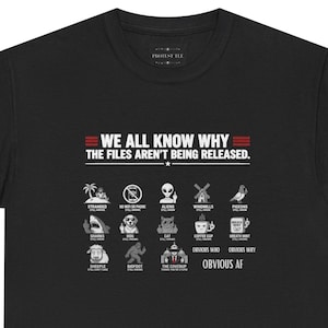 Może przedstawiać: Czarny t-shirt z białym nadrukiem graficznym z tekstem WE ALL KNOW WHY THE FILES AREN'T BEING RELEASED. Poniżej znajdują się ikony palmy, telefonu, kosmity, wiatraka, gołębia, rekina, psa, kota, filiżanki kawy, mięty, owcy i Wielkiej Stopy.