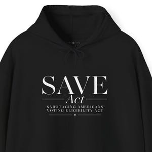 Peut inclure: Un sweat-shirt à capuche noir avec le texte blanc SAVE Act, suivi du sous-titre Sabotaging Americans Voting Eligibility Act imprimé en plus petit, le tout agrémenté de lignes horizontales décoratives et d'une petite étoile.