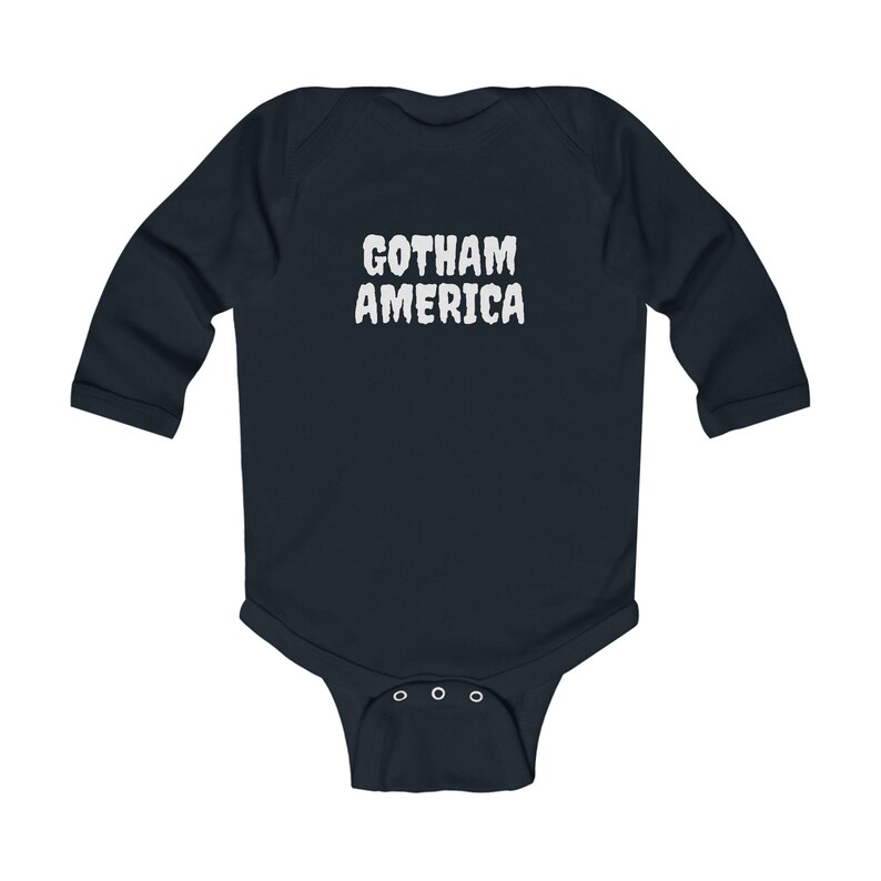 K&ouml;nnte beinhalten: Ein marineblaues Baby-Body mit langen &Auml;rmeln und dem wei&szlig;en Text "GOTHAM AMERICA" auf der Brust. Der Body hat einen Druckknopfverschluss am unteren Ende und ist aus weichem Material gefertigt.