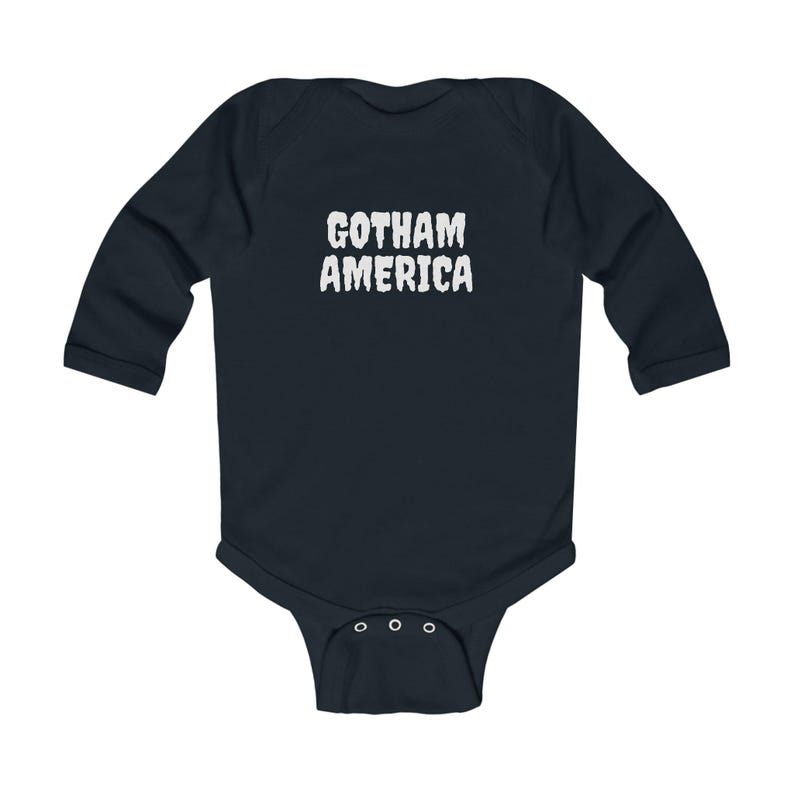 K&ouml;nnte beinhalten: Ein marineblaues Baby-Body mit langen &Auml;rmeln und dem wei&szlig;en Text "GOTHAM AMERICA". Der Body hat einen Druckknopfverschluss am unteren Ende und ist aus weichem Material gefertigt.