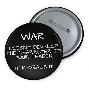 May include: A black button with the word "WAR" in white, followed by the text "DOESN'T DEVELOP THE CHARACTER OF YOUR LEADER IT REVEALS IT." The button has a silver pin back.
