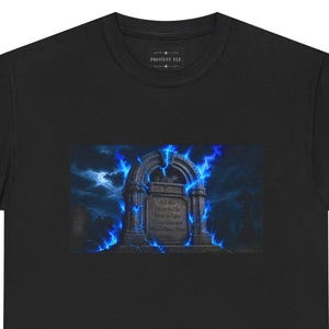Może przedstawiać: Czarny t-shirt z grafiką przedstawiającą kamienny nagrobek otoczony jarzącymi się niebieskimi płomieniami pod rozgwieżdżonym niebem w świetle księżyca. Na nagrobku widnieje napis: All We Have to Do Now is Take These Lies and Make Them True.