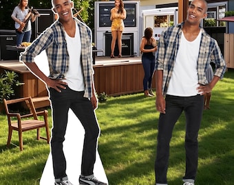 May include: A life-size cardboard cutout of a man wearing a white t-shirt, a blue and tan plaid shirt, black jeans, and gray sneakers. The cutout is posed on a green lawn with a stage and people in the background.