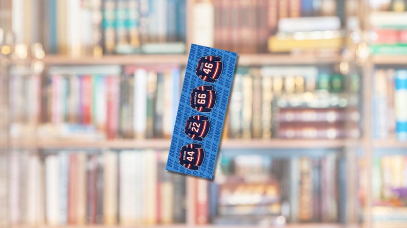 Op de afbeelding: Een blauwe boekenlegger met vier hockeytrui-ontwerpen met de nummers 44, 22, 66 en 46. De tekst "OFF-CAMPUS" is verticaal afgedrukt. De achtergrond is een vage boekenkast.