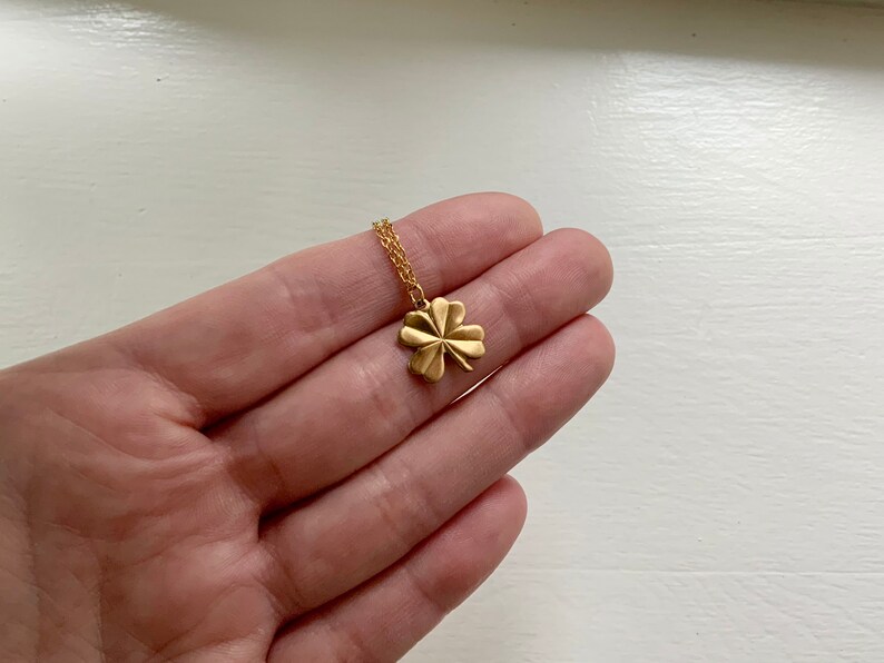 May include: A gold four-leaf clover pendant necklace on a delicate chain.