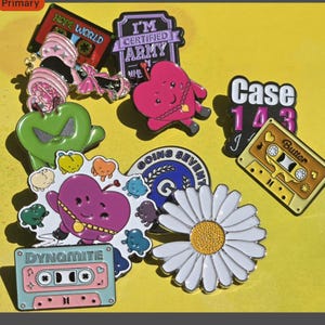 Puede incluir: Una colección de coloridos pines esmaltados con varios diseños, incluyendo una margarita, un corazón y cintas de cassette. Los pines presentan textos como "HOPE WORLD", "I'M CERTIFIED ARMY", "Case 143", "Butter" y "Dynamite".