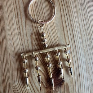 May include: A gold-colored, handmade dream catcher with a circular ring and dangling beads and cone-shaped pendants. The dream catcher is displayed on a wooden surface.