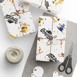 May include: Graduation-themed gift-wrapped presents with gold stars, mortarboards, and diplomas on white paper. Each package is tied with twine and a white tag. A ball of twine, scissors, and blank tags are also visible.