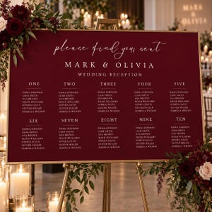 Puede incluir: Un cartel rectangular de color rojo intenso para la distribución de asientos de una boda con un marco dorado fino. El texto dice "please find your seat", "MARK & OLIVIA", "WEDDING RECEPTION" y enumera las mesas del uno al diez.