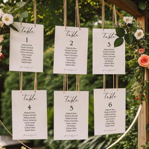 Può includere: Sei cartellini rettangolari bianchi per il tableau de mariage appesi a cordini di juta. Ogni cartellino riporta la parola Table seguita da un numero da uno a sei, un elenco di nomi e il testo please find your seat in nero.