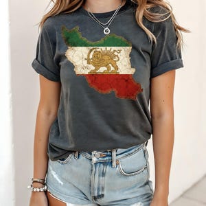 Puede incluir: Camiseta gris oscuro con un gr&aacute;fico desgastado de la bandera iran&iacute; en forma del pa&iacute;s. El dise&ntilde;o de la bandera incluye rayas verdes, blancas y rojas con un emblema de le&oacute;n y sol dorado.