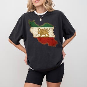Puede incluir: Camiseta negra con un gr&aacute;fico desgastado de la bandera iran&iacute; en un contorno de mapa. El dise&ntilde;o incluye secciones verdes, blancas y rojas con un emblema de le&oacute;n y sol. La camiseta tiene cuello redondo y mangas cortas.