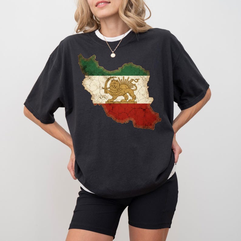 Puede incluir: Camiseta negra con un gr&aacute;fico desgastado de la bandera iran&iacute; en un contorno de mapa. El dise&ntilde;o incluye secciones verdes, blancas y rojas con un emblema de le&oacute;n y sol. La camiseta tiene cuello redondo y mangas cortas.