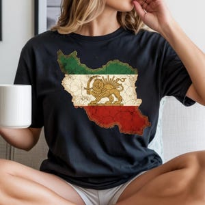 Puede incluir: Camiseta negra con un gr&aacute;fico desgastado de la bandera iran&iacute; en forma de mapa. El dise&ntilde;o de la bandera incluye rayas verdes, blancas y rojas, con un emblema de le&oacute;n y sol dorado en el centro. Es una prenda de vestir informal.