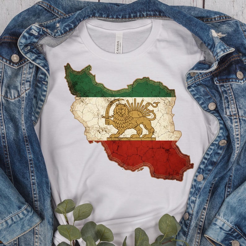 Puede incluir: Camiseta blanca con un gr&aacute;fico desgastado del mapa de Ir&aacute;n con los colores de la bandera nacional. El dise&ntilde;o incluye un le&oacute;n sosteniendo una espada, con secciones verdes y rojas. La camiseta est&aacute; debajo de una chaqueta vaquera.
