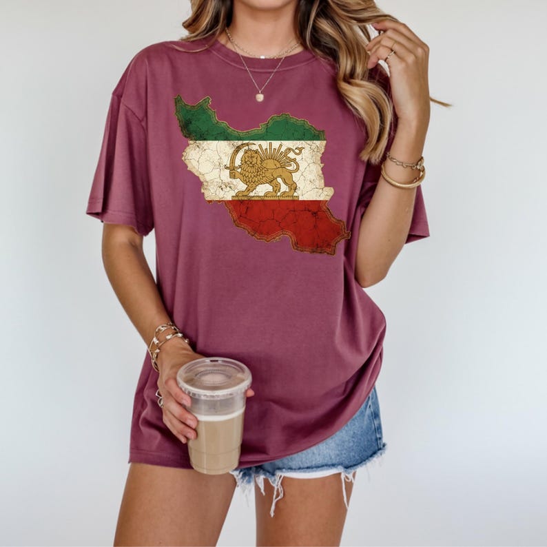 Puede incluir: Camiseta burdeos con un gr&aacute;fico desgastado de la bandera iran&iacute; en forma de mapa. El dise&ntilde;o de la bandera incluye rayas verdes, blancas y rojas con un emblema de le&oacute;n y sol dorado. La camiseta tiene mangas cortas y un corte holgado.