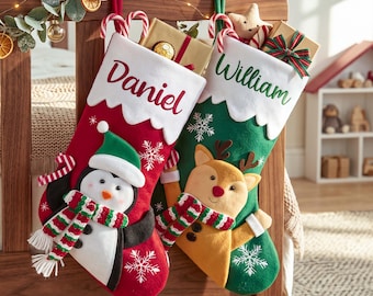 Puede incluir: Dos calcetines navideños con puños blancos que llevan los nombres Daniel y William. El calcetín rojo muestra un pingüino con gorro y bufanda verdes, mientras que el verde presenta un reno con nariz roja y una bufanda a rayas.