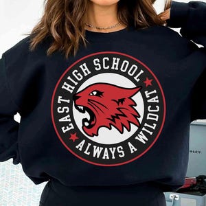 Può includere: Felpa nera con grafica circolare con la scritta "EAST HIGH SCHOOL ALWAYS A WILDCAT". Il design presenta una testa di gatto selvatico rossa con dettagli bianchi e rossi. Girocollo.