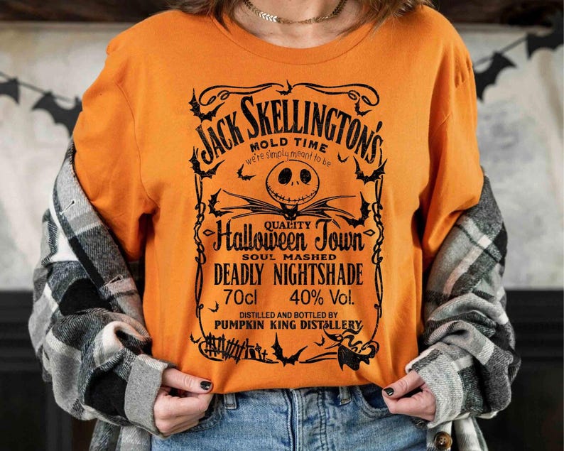 May include: Orange long-sleeve shirt with a black graphic featuring Jack Skellington's name and a Halloween-themed design. The text includes "Halloween Town" and "Deadly Nightshade". The shirt also has "70cl" and "40% Vol." printed on it.