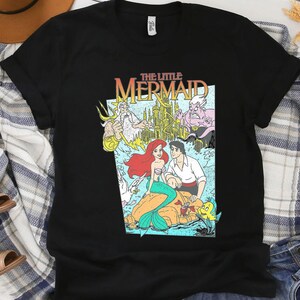 Puede incluir: Camiseta negra con un gr&aacute;fico colorido de La Sirenita de Disney. El dise&ntilde;o incluye a Ariel, el Pr&iacute;ncipe Eric y otros personajes, con el t&iacute;tulo en una fuente retro. Una camiseta cl&aacute;sica para los fans de la pel&iacute;cula animada.