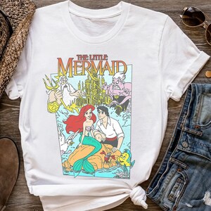 Puede incluir: Camiseta blanca con un gr&aacute;fico colorido de "La Sirenita". El dise&ntilde;o incluye a Ariel, el Pr&iacute;ncipe Eric, el Rey Trit&oacute;n y &Uacute;rsula, con el t&iacute;tulo de la pel&iacute;cula en una fuente vibrante. La camiseta es de estilo cuello redondo cl&aacute;sico.