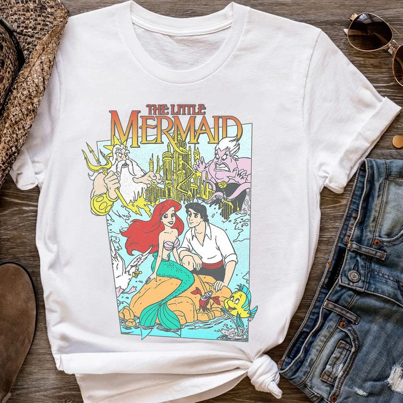 Puede incluir: Camiseta blanca con un gr&aacute;fico colorido de "La Sirenita". El dise&ntilde;o incluye a Ariel, el Pr&iacute;ncipe Eric, el Rey Trit&oacute;n y &Uacute;rsula, con el t&iacute;tulo de la pel&iacute;cula en una fuente vibrante. La camiseta es de estilo cuello redondo cl&aacute;sico.