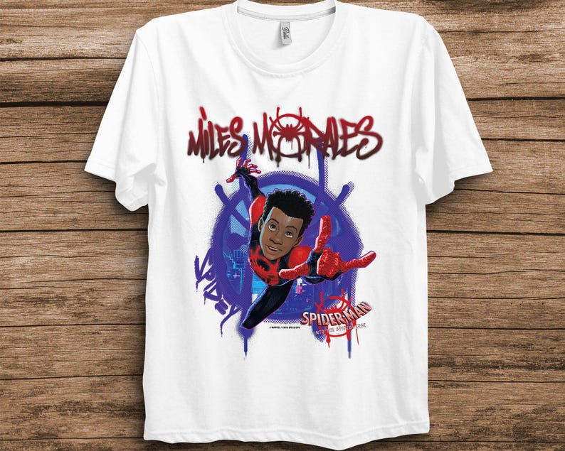 May include: A white short-sleeved t-shirt featuring a graphic of Miles Morales in a red and black suit. The text "MILES MORALES" appears in a red graffiti style above, with "SPIDER-MAN INTO THE SPIDER-VERSE" printed in the lower right corner.