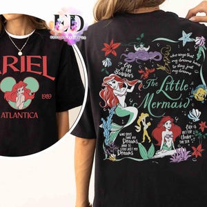 May include: A black t-shirt featuring a front graphic with the text ARIEL EST. 1989 ATLANTICA and an illustration of Ariel. The back graphic displays The Little Mermaid, Ariel, Flounder, and text including Life is the Bubbles and Life is Better Under the Sea.
