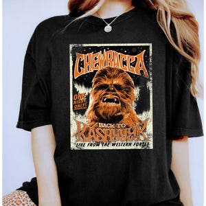 May include: Black t-shirt with a retro poster design. The poster features the word "Chewbacca" in orange, and an image of Chewbacca. The poster also includes the text "Back to Kashyyyk" and "Live from the Western Forest."