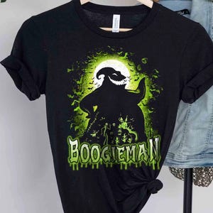 Pode incluir: Camiseta preta com um design gr&aacute;fico verde e branco de um personagem em frente a uma lua cheia, com morcegos e a palavra "BOOGIEMAN". O design tem um tema de Halloween. &Eacute; uma camiseta gr&aacute;fica.