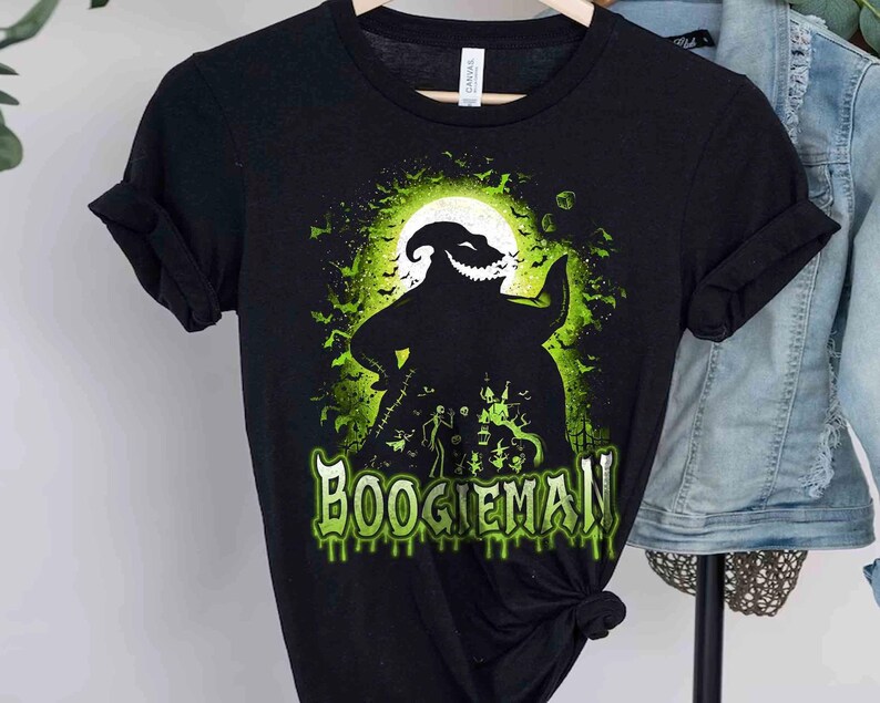 Pode incluir: Camiseta preta com um design gr&aacute;fico verde e branco de um personagem em frente a uma lua cheia, com morcegos e a palavra "BOOGIEMAN". O design tem um tema de Halloween. &Eacute; uma camiseta gr&aacute;fica.