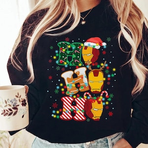 May include: Black sweatshirt with a festive "Ho Ho Ho" design featuring Iron Man's helmet and Christmas elements. The letters are decorated with lights, candy canes, and snowflakes, creating a holiday theme.