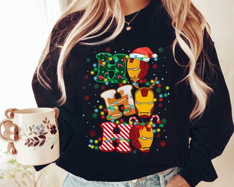 May include: Black sweatshirt with a festive "Ho Ho Ho" design featuring Iron Man's helmet and Christmas elements. The letters are decorated with lights, candy canes, and snowflakes, creating a holiday theme.