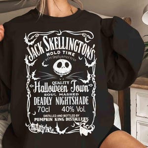 May include: Black sweatshirt featuring a white graphic design with the text "Jack Skellington's Mold Time" and "Halloween Town". The design includes a skull, bats, and other Halloween-themed elements. The sweatshirt also has the text "Deadly Nightshade" and "70cl 40% Vol."