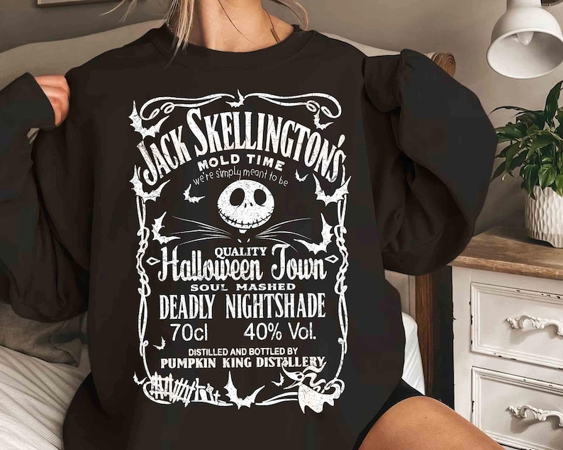 May include: Black sweatshirt featuring a white graphic design with the text "Jack Skellington's Mold Time" and "Halloween Town". The design includes a skull, bats, and other Halloween-themed elements. The sweatshirt also has the text "Deadly Nightshade" and "70cl 40% Vol."