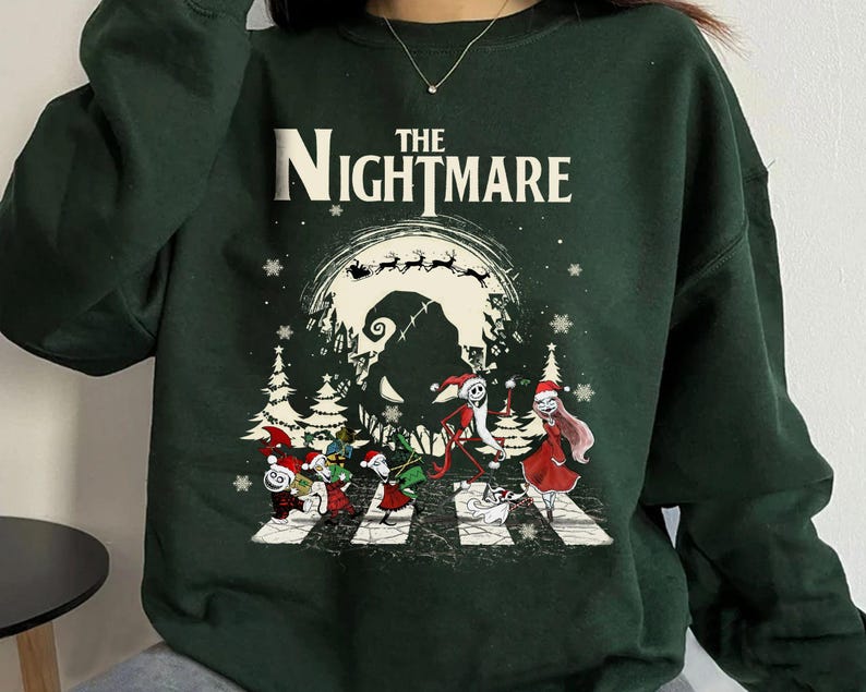 Pode incluir: Camisola verde escuro com um gr&aacute;fico de "O Estranho Mundo de Jack". O design apresenta personagens atravessando uma faixa de pedestres, uma lua assustadora e as palavras "The Nightmare" em branco. Flocos de neve e &aacute;rvores de Natal tamb&eacute;m s&atilde;o vis&iacute;veis.