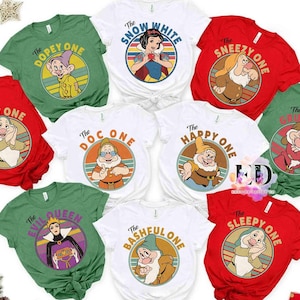 May include: A collection of short-sleeved t-shirts in various colors, each featuring a different character from a classic animated film. The shirts display characters like Snow White and the seven dwarfs, with their names printed above.
