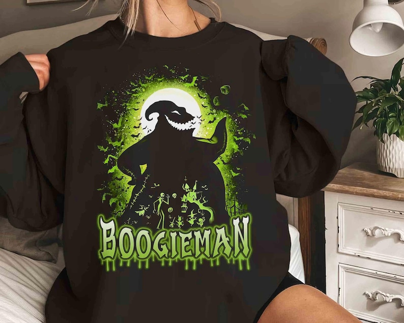 Pode incluir: Camisola preta com um gr&aacute;fico verde e preto do Boogieman de O Estranho Mundo de Jack. O design apresenta a silhueta da personagem contra uma lua cheia, com "BOOGIEMAN" em verde com letras gotejantes.